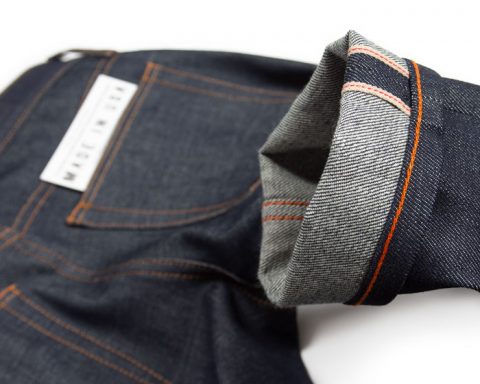 Hem of American-made raw denim selvedge jeans with orange chain stitch hemming shows what is aw denim, selvedge on jeans and chain stitching.