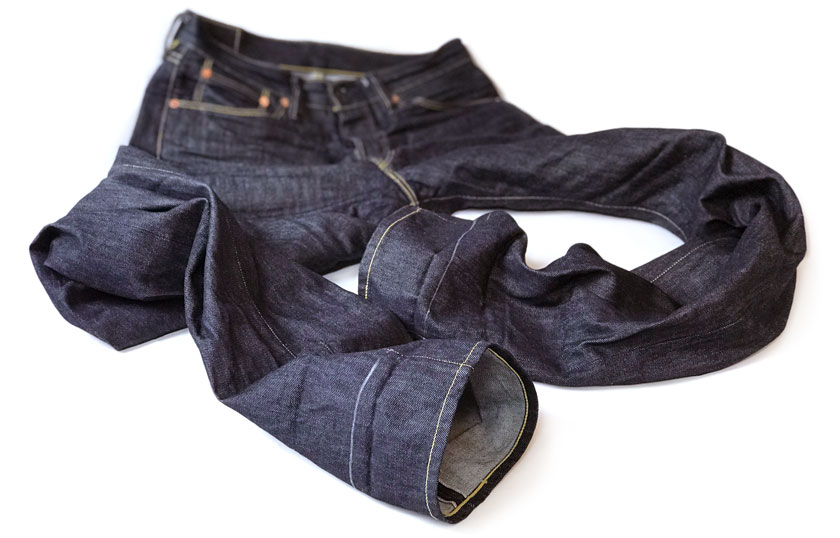 A pair of raw denim LeRoy Strauss jeans are shown at their original length, and a chalk line marks the hemming cut line.