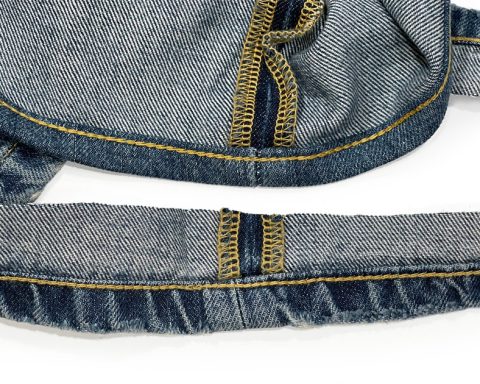 A close-up of professional chain stitch hemming alterations highlights what chain stitching is by displaying a thick golden yellow chain stitch on the hem of blue jeans.