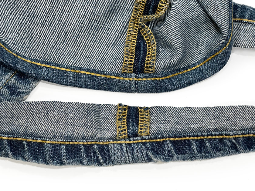 A close-up of professional chain stitch hemming alterations highlights what chain stitching is by displaying a thick golden yellow chain stitch on the hem of blue jeans.