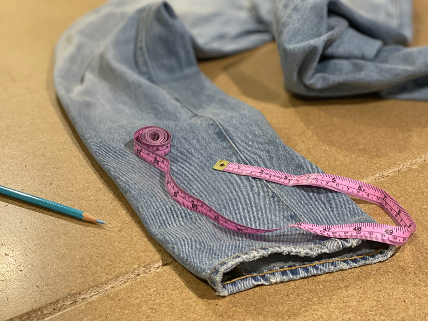 The leg opening of a pair of jeans is shown on a table, indicating how the inseam of jeans with twisted legs is about to be measured. The chain-stitched hem has a roping effect as well.