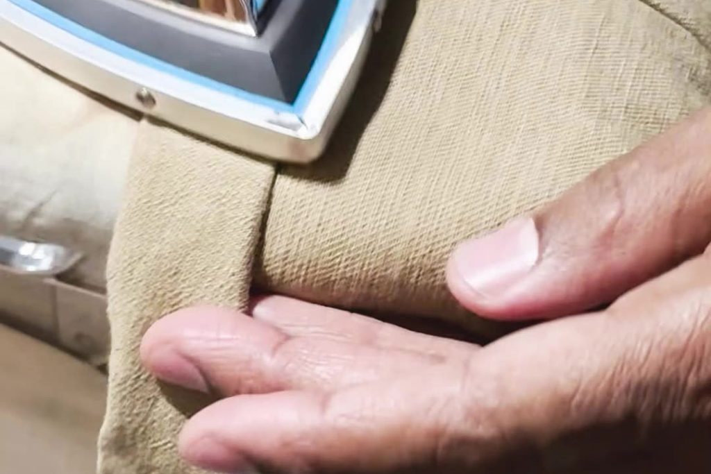 Close-up of professional pant hemming, showing the pressing process after sewing. The image is part of a video tutorial by Denimbmc.com on how to hem pants correctly.