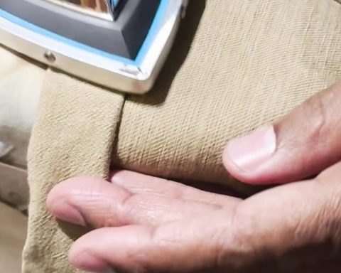 Close-up of professional pant hemming, showing the pressing process after sewing. The image is part of a video tutorial by Denimbmc.com on how to hem pants correctly.