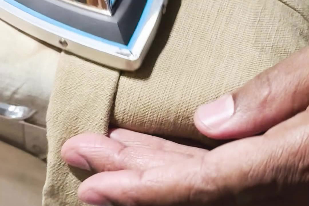 Close-up of professional pant hemming, showing the pressing process after sewing. The image is part of a video tutorial by Denimbmc.com on how to hem pants correctly.