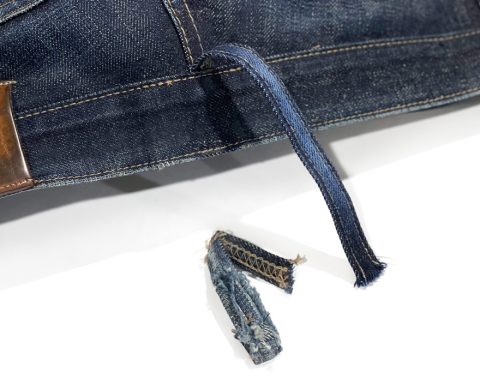 A pair of jeans showing a newly attached replacement belt loop beside the original worn, detached loop, highlighting professional repair work by the Williamsburg Garment Company's belt loop repair service.