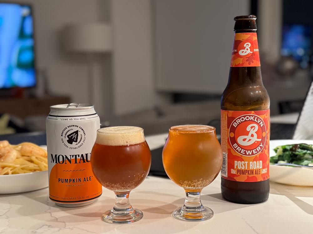 Two glasses on a table, left filled with Montauk Pumpkin Ale showing a darker hue and creamier head, right filled with Brooklyn Brewery Post Road Pumpkin Ale, lighter in color.