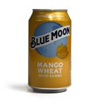 A can of Blue Moon Mango Wheat beer, photographed on a white background, for a Denimbmc.com blog review. The can features bright yellow-orange packaging with a mango illustration.