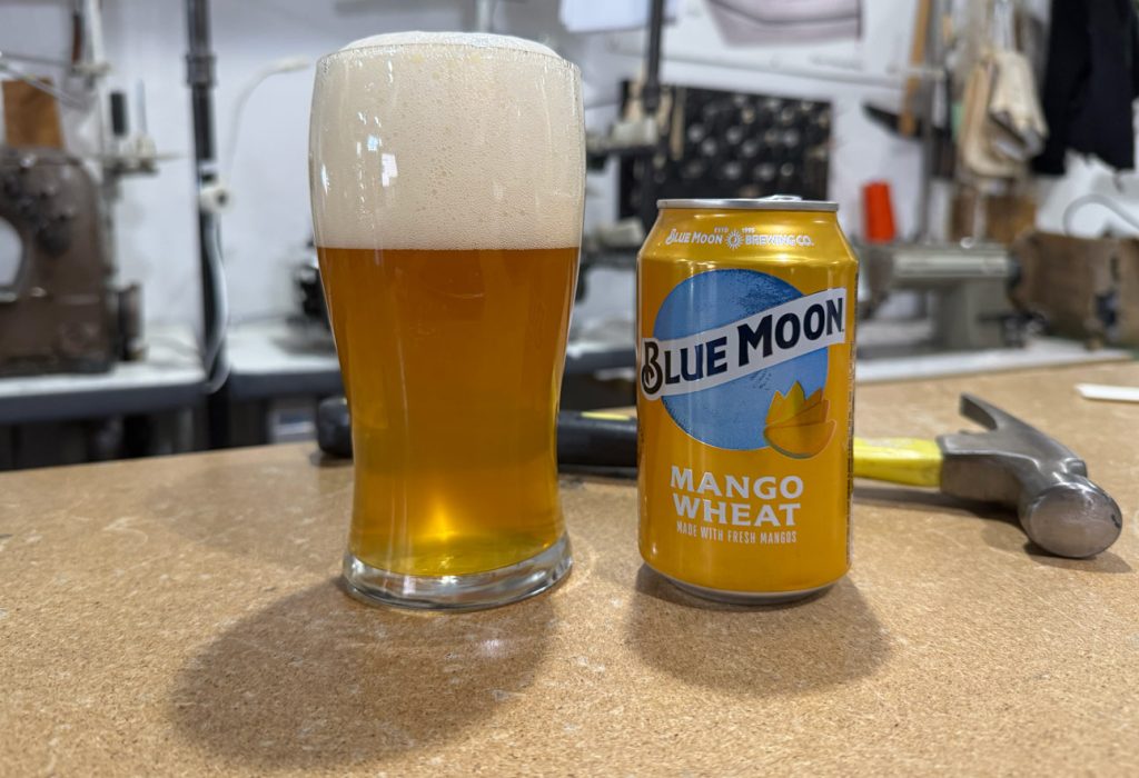 A glass of Blue Moon Mango Wheat beer with a can beside it, taken inside the Williamsburg Garment Company studio to showcase how the beer pours and looks.