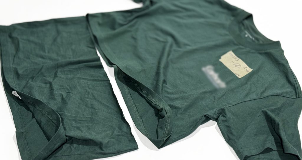 An example of Williamsburg Garment Company's professional t-shirt hemming service on a green cropped t-shirt shows the coverstitched sewing and shortened lower half of the cut-away part of the tee for before and after review.